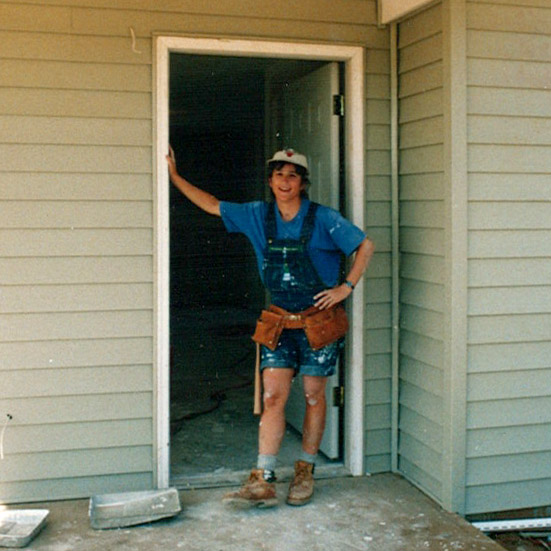 Karen wearing a tool belt standing in doorway of home.